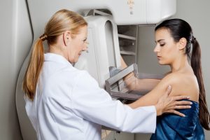 Mature female doctor assisting young patient undergoing mammogram